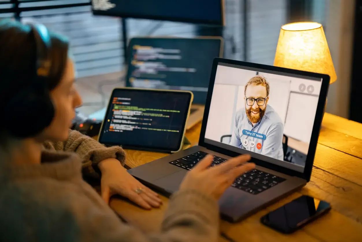 The picture presents a person sitting at the computer and video conferences with someone visible on the screen. A person on the other side smiles and looks like a technical person