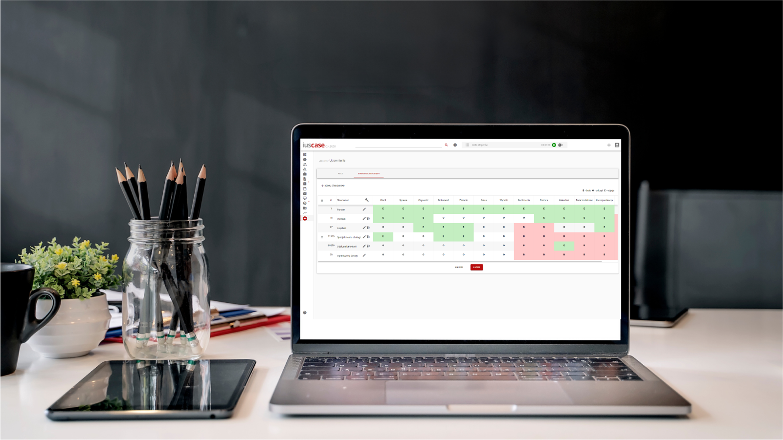 The image features a laptop on a desk with office supplies and the legal services management app open on the screen. The app interface displays a grid or table with data highlighted in green and red.