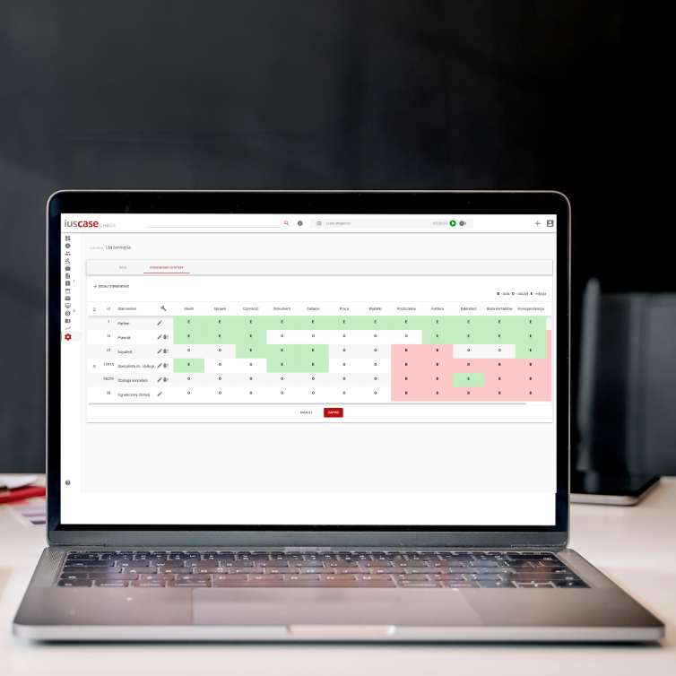 A close-up view of a laptop on a desk showing the legal services management app interface. The screen displays a grid or table with various data entries highlighted in green and red.